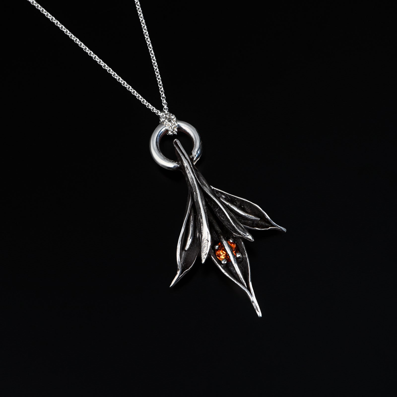 Silver pendant with leaves and a small orange gemstone on a black background
