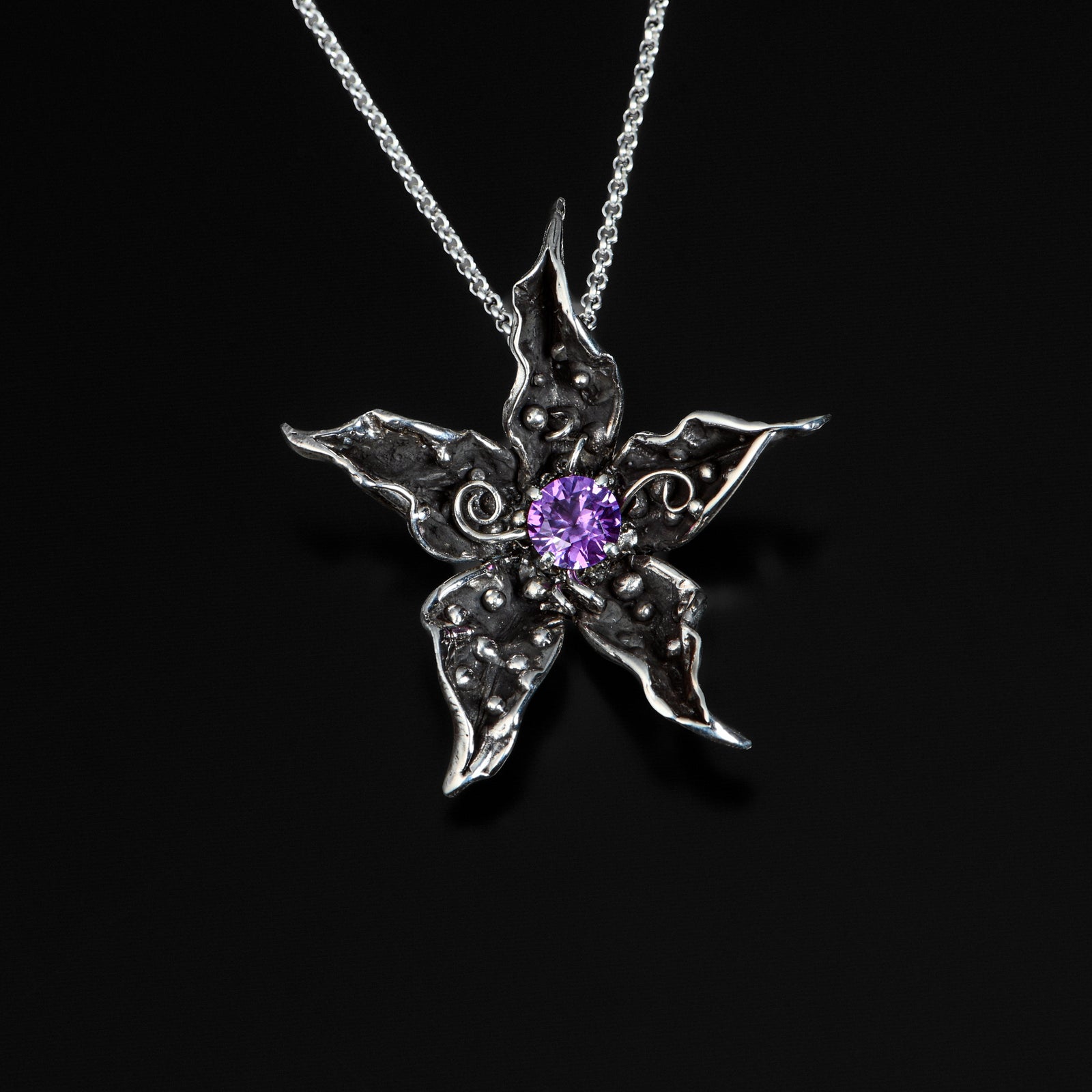 Silver pendant with a purple gemstone on a black background