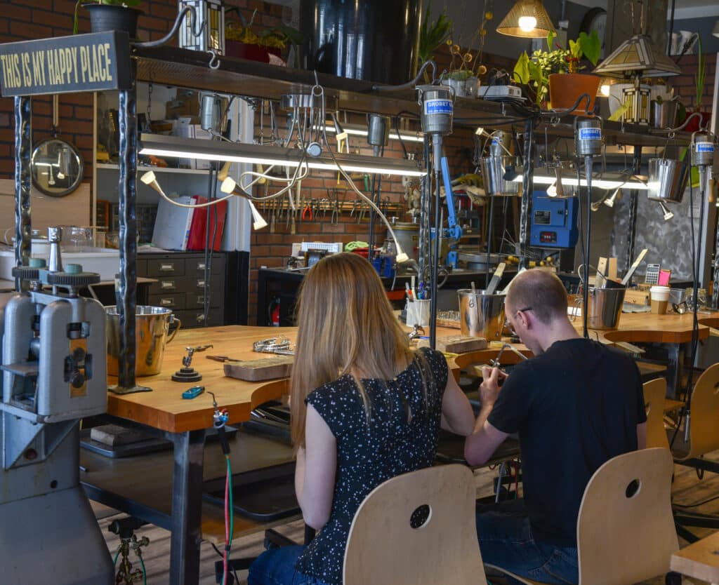 A couple making their wedding rings side by side at the Juvelisto studio bench